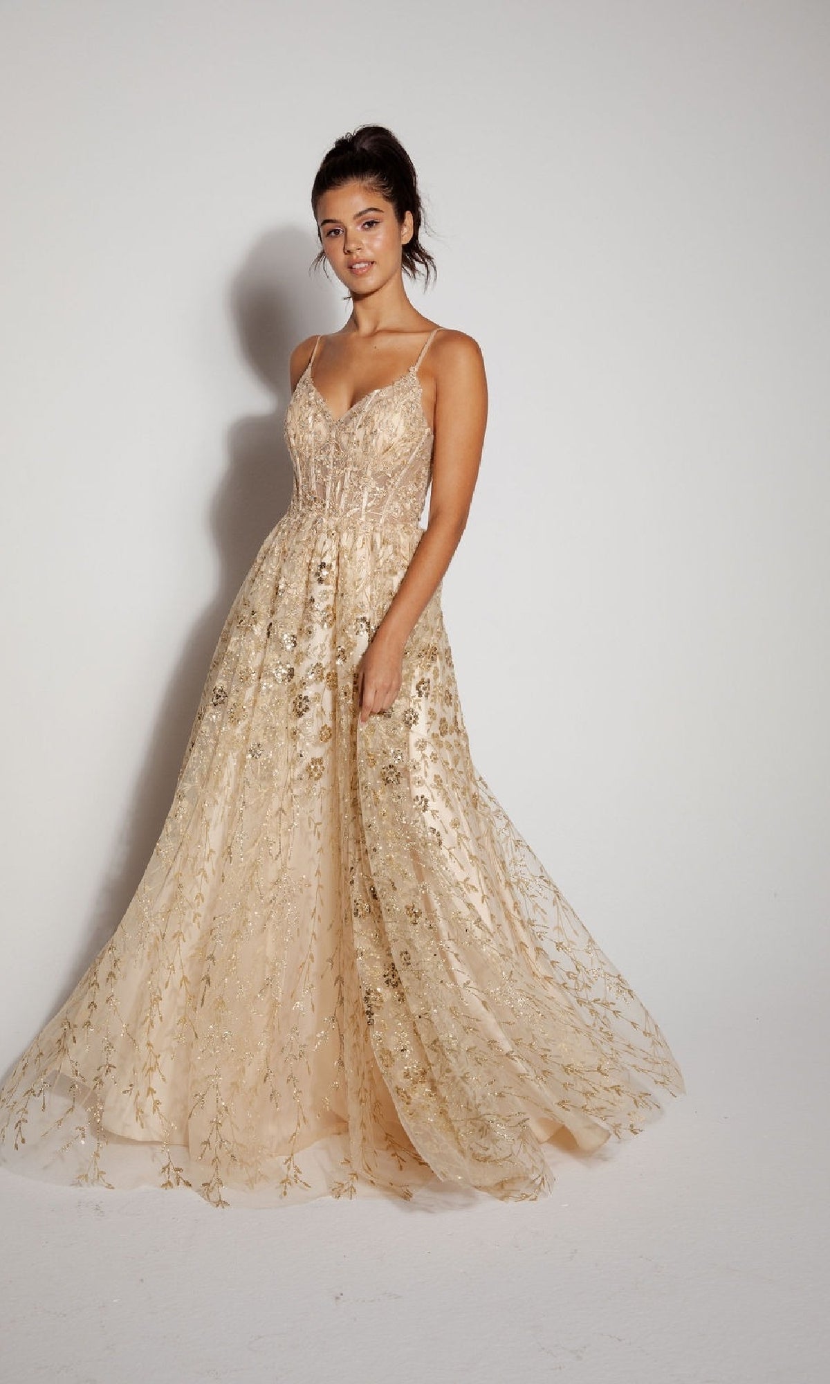 A woman models the Eureka 9908 Long Glitter A-Line Prom Dress, featuring thin straps, floral embroidery, and sequin embellishments in light beige, standing against a plain white background.